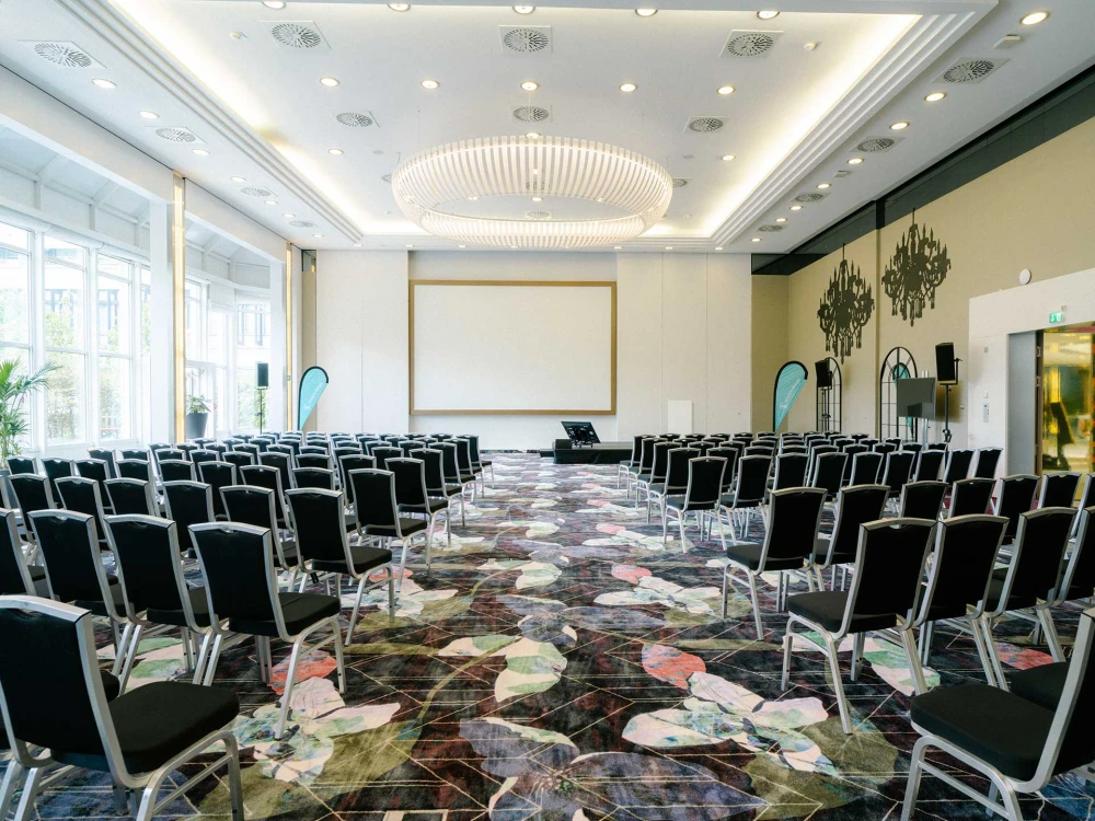 Eleganter Konferenzraum mit moderner Bestuhlung, großer Leinwand und stilvoller Beleuchtung, ideal für Tagungen, Seminare und Präsentationen.