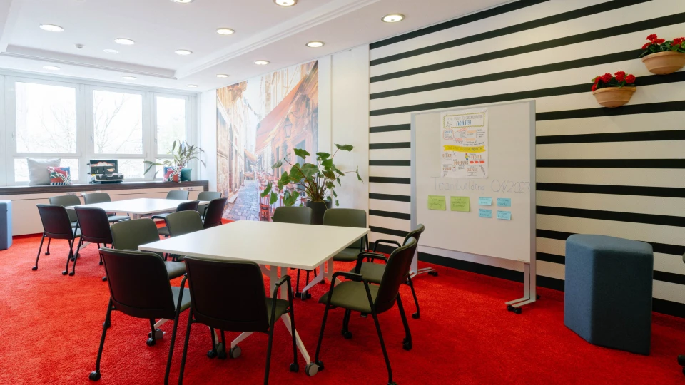 Konferenzraum mit schwarz-weißen Streifenwänden, roten Teppichen, weißen Tischen, Pinnwand mit Notizen und Wanddekorationen