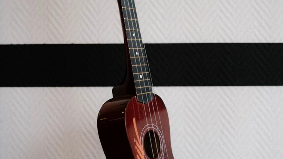 Hängende Ukulele mit der Aufschrift 'Hawaii' vor einer schwarz-weiß gestreiften Wand
