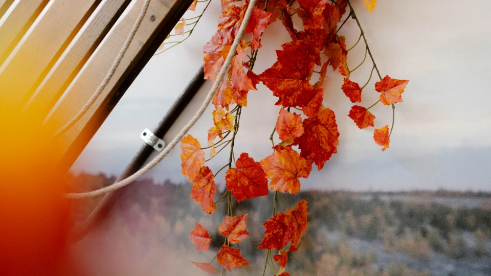 Holzschlitten mit herabhängender Dekoration aus roten Herbstblättern vor einem Landschaftsbild mit Rentiermotiv