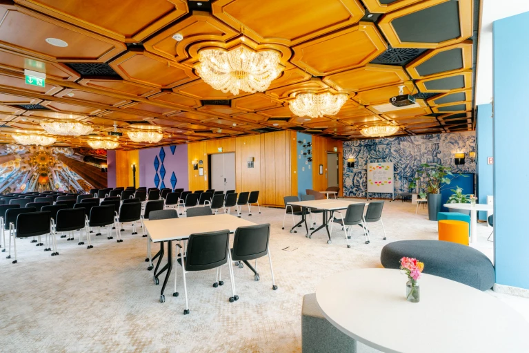 Großer Konferenzraum mit Holzkassettendecke, Kronleuchtern, schwarzen Stühlen, runden Tischen und einer kreativen Wandgestaltung