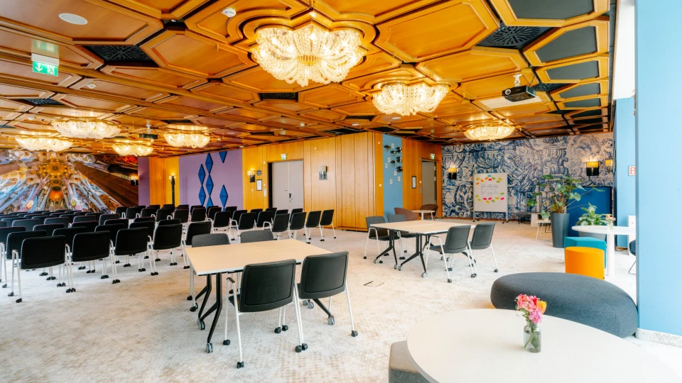 Großer Konferenzraum mit Holzkassettendecke, Kronleuchtern, schwarzen Stühlen, runden Tischen und einer kreativen Wandgestaltung