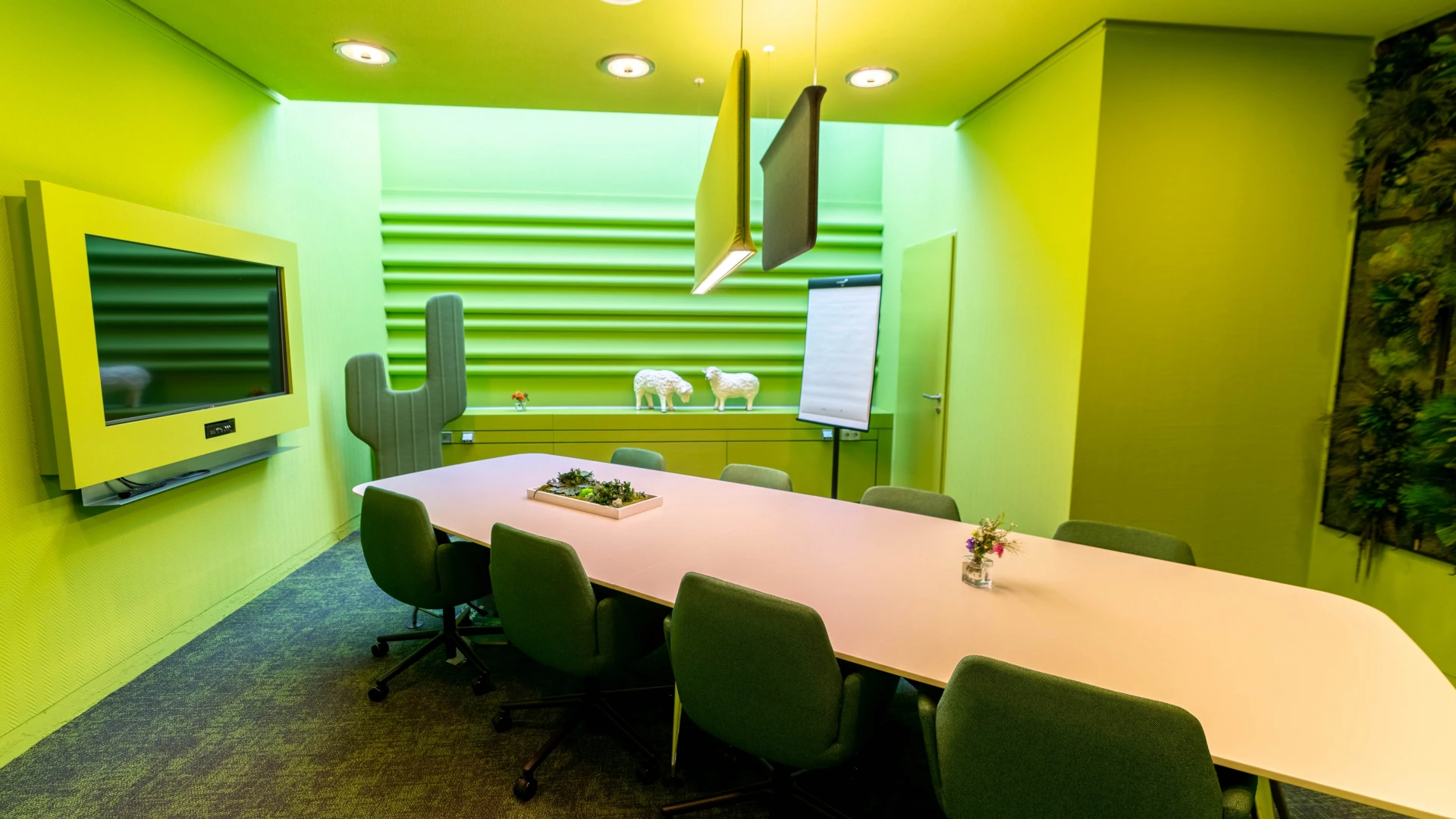 Moderner Meetingraum mit grünen Wänden, Akustikelementen, großem Konferenztisch und dekorativen Schaf-Figuren