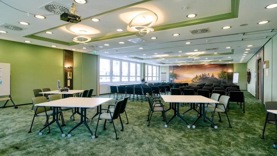 Moderner Konferenzraum mit grünen Wänden, flexibler Bestuhlung, stilvollen Deckenleuchten und großem Landschaftswandbild