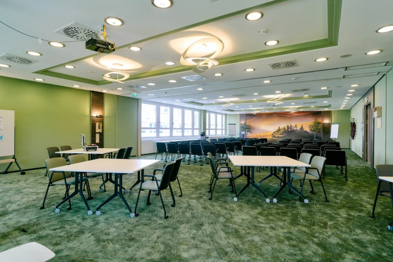 Moderner Konferenzraum mit grünen Wänden, flexibler Bestuhlung, stilvollen Deckenleuchten und großem Landschaftswandbild