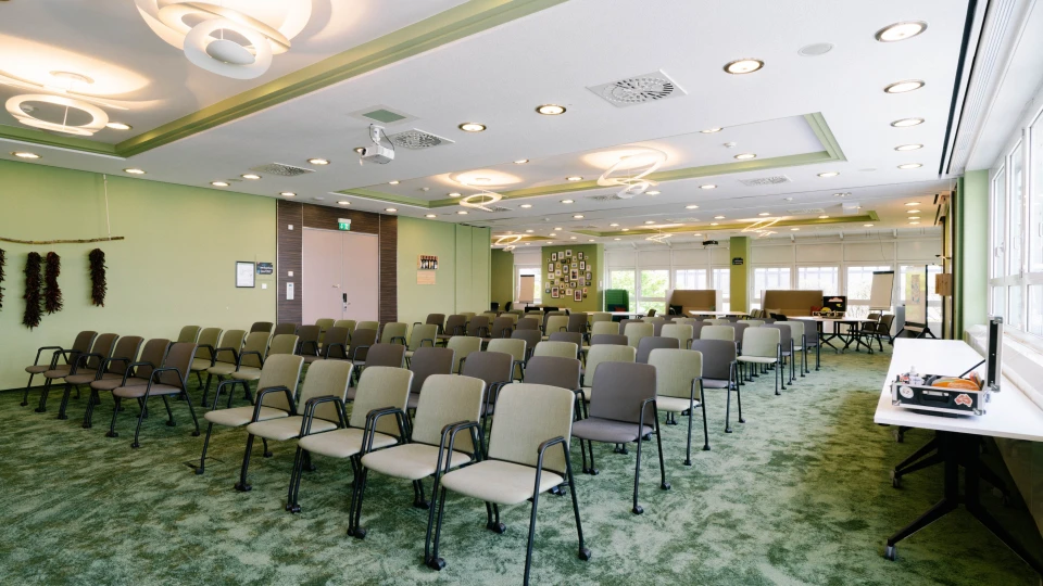 Heller Konferenzraum mit grüner Teppichgestaltung, moderner Deckenbeleuchtung und flexibler Bestuhlung für Veranstaltungen