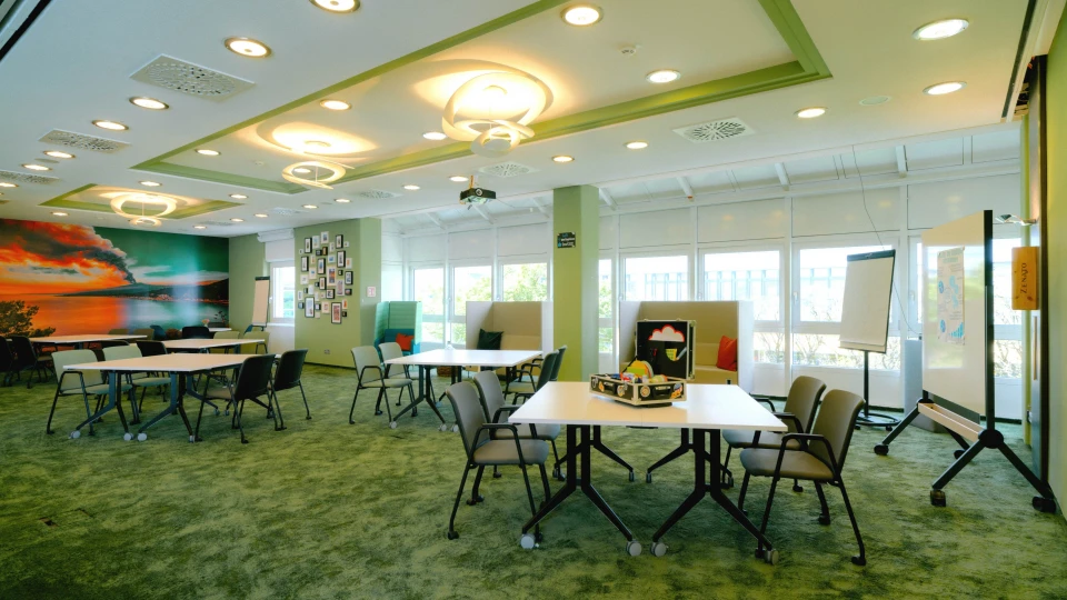 Heller, flexibel gestaltbarer Konferenzraum mit grüner Farbgestaltung, modernen Deckenleuchten und einer großflächigen Natur-Fototapete