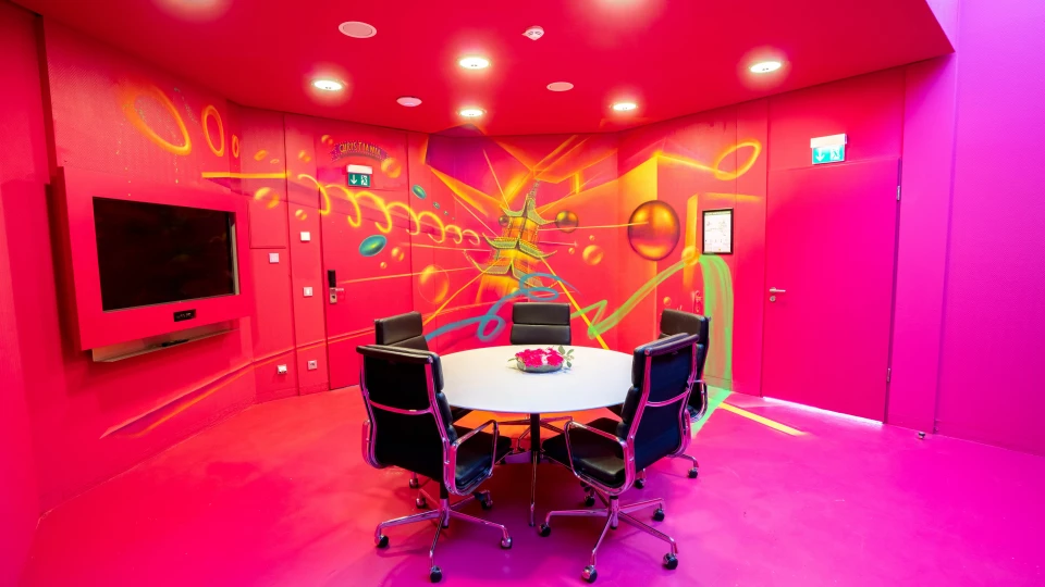 Kreativer Besprechungsraum mit neonfarbigen Wandmotiven, schwarzem Konferenzstuhl-Set und moderner technischer Ausstattung