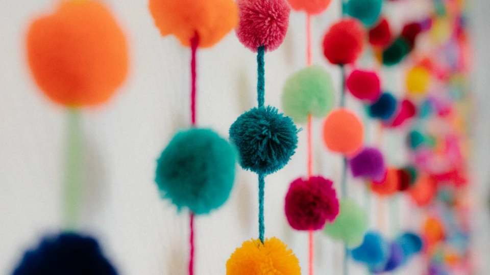 Bunte Pompon-Girlanden hängen an einer Wand und sorgen mit kräftigen Farben für eine fröhliche Raumgestaltung