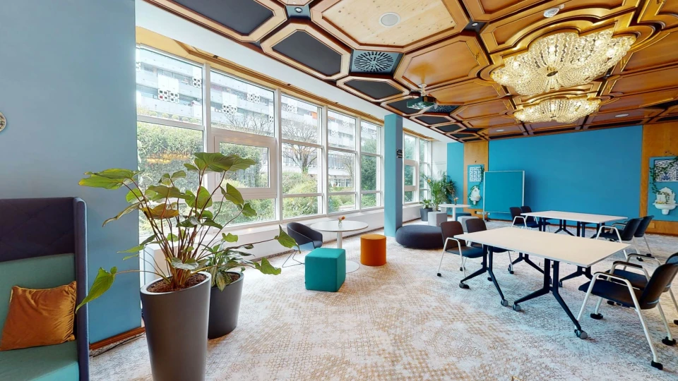 Offener Meetingraum mit blauen Akzenten, Kronleuchtern und flexiblen Sitzmöglichkeiten für kreativen Austausch