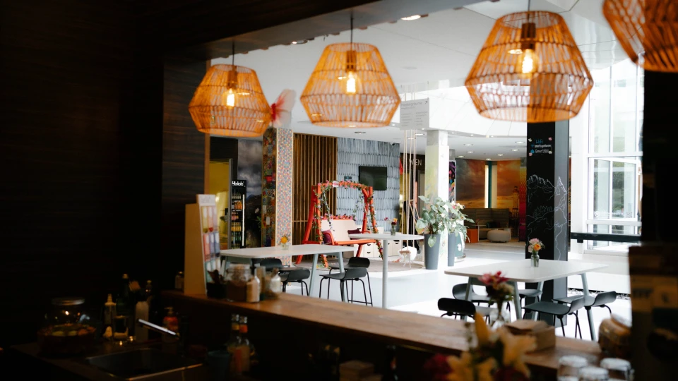 Innenansicht des Cafés mit Blick auf Theke, Hängelampen aus Korbgeflecht und Gemeinschaftstischen