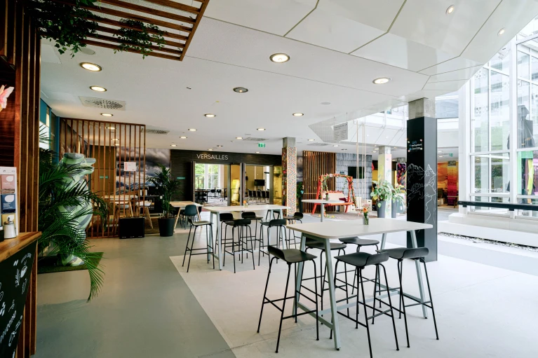 Heller Cafébereich mit Stehtischen, Hockern und Blick auf Besprechungsräume und Schaukelbank