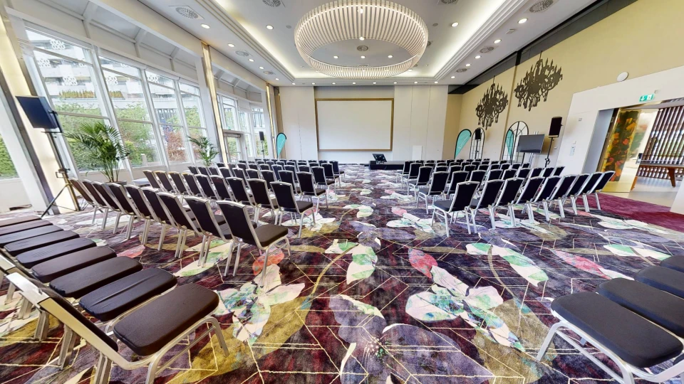 Tagungsraum Wien mit Kinobestuhlung, großer Leinwand und dekorativen Kronleuchter-Applikationen an der Wand.