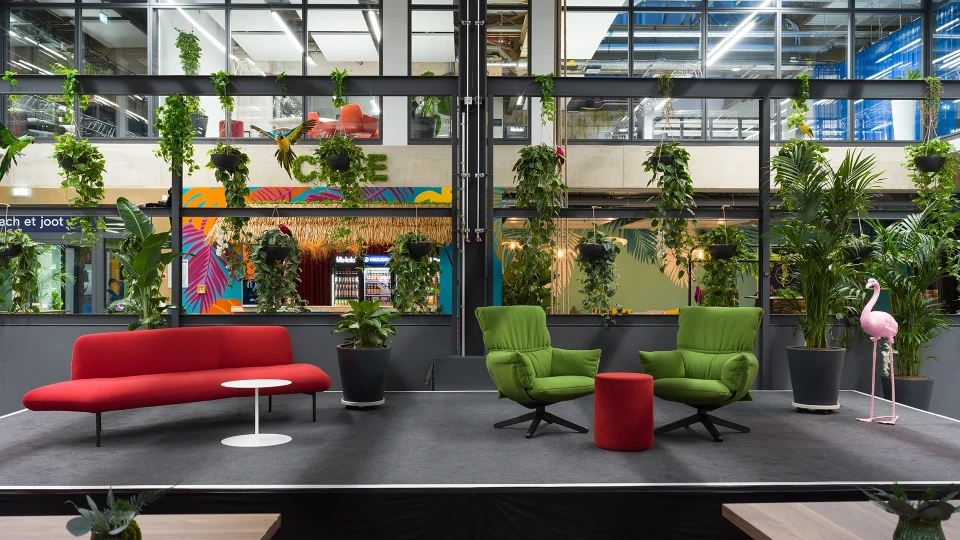 Moderne Loungefläche mit rotem Sofa, grünen Sesseln und tropischer Bepflanzung im smartvillage Köln